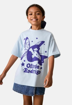 Lyseblå oversized t-shirt med lilla sommerfuglegrafik og teksten "Olivia Rodrigo", korte ærmer og rund halsudskæring.