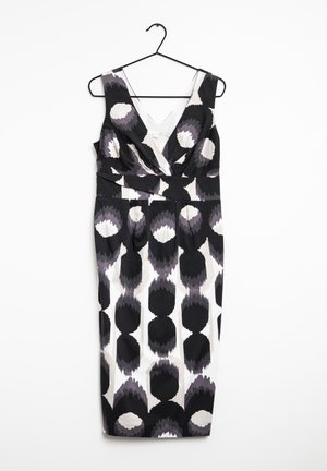Robe noire et blanche sans manches, longueur aux genoux, décolleté en V profond avec motif circulaire abstrait, suspendue à un cintre en fil noir.