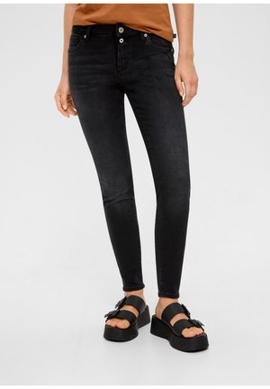Jean en denim noir slim fit avec un léger éclat, fermeture à bouton, cinq poches et taille mi-haute, associés à des sandales à plateforme noires.