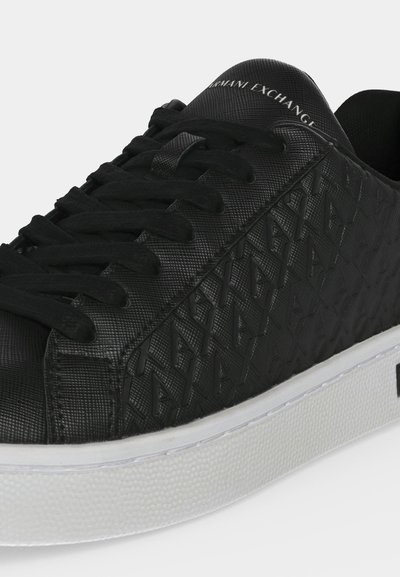 Gros plan sur une basket noire Armani Exchange avec des lacets noirs, des côtés texturés à motif de logo et une semelle blanche épaisse.