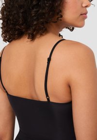 Zwarte cami met dunne verstelbare banden, met een gladde, zachte textuur en een getailleerd ontwerp, dat de huid op de rug laat zien.
