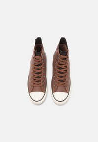 Baskets montantes en cuir marron avec accents noirs, embouts en caoutchouc blanc et œillets métalliques. Les lacets sont marron avec des détails cousus.