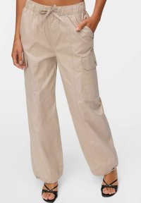 Beige cargobroek met een elastische tailleband, trekkoord en zijzakken. Losse pasvorm met een iets taps toelopende pijp en ritsaccenten op de boorden.