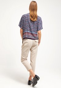 Tummansinisellä kukkakuosisella puserolla, jossa on lyhyet hihat, yhdistetty vaaleanbeigeihin kapeneviin housuihin. Asusteessa on tummanvärinen helma ja yksiväriset mustat kengät.