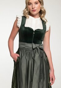 Traditional green dirndl dress with ruffled white blouse. Features a zip front, tied waist, and textured fabric with a subtle pattern.