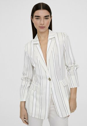 Blazer blanco con rayas verticales negras, cierre de un solo botón y dos bolsillos frontales. Tejido ligero, hombros estructurados y mangas enrolladas.