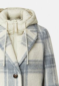 Cappotto in misto lana con cappuccio imbottito staccabile color crema, fantasia a quadri blu e bianco, ampi risvoltini e chiusura frontale con bottoni.