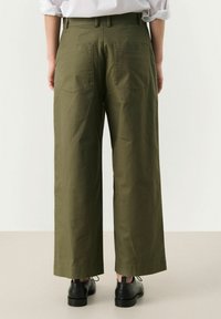 Olijfgroene wijde broek van katoen, met twee achterzakken en een soepele textuur. Zwarte schoenen met veters maken de outfit compleet.
