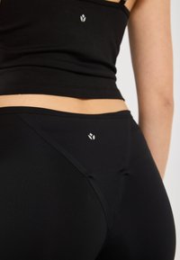 Svart treningsklær med en tettsittende crop top og høytaljede leggings, laget av glatt stoff med en liten logo på baksiden.