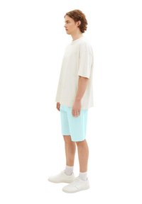 Cream oversized t-shirt, light blue shorts, and white sneakers. Casual fit, cotton material, short sleeves, and crew neck design.