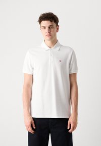 Hvid polo t-shirt lavet af bomuld, med krave og korte ærmer. Lille rødt logo på venstre bryst, enkelt design.