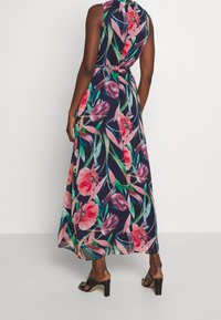 Maxiklänning med blommönster i rosa, grönt och marinblått. Ärmlös design med bälte i midjan. Smooth tyg och flödande silhuett.