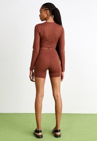Smeđi, dugosleeve crop top uparen s odgovarajućim visokim hlačama, izrađen od rastezljivog materijala, s glatkom teksturom i prilagođenim dizajnom.
