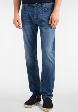 Jeans in denim a taglio slim di colore blu medio con lievi scoloriture. Design classico a cinque tasche, rivetti metallici e cuciture a contrasto. Abbinati a calzature scure.