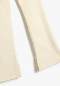 Pantalones de algodón crema con forma acampanada, que presentan aberturas laterales y una textura acanalada. La tela es suave y ligera.