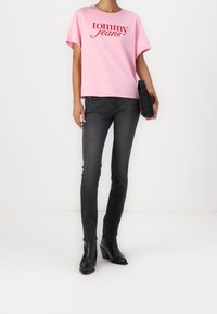 Růžové bavlněné tričko s nápisem "tommy jeans" v červeném tisku, kombinované s černými skinny džíny a černými vyššími kotníkovými botami na podpatku. Jednoduchý design, úzký střih.