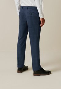 Navy plaid dress pants with a tailored fit, featuring back pockets and black shoes with brown sole accents. Smooth fabric texture.