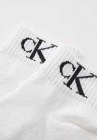 Calzini bianchi in cotone con bordino a costine e il logo "ck" ricamato in nero su un lato. Texture liscia con un design classico a lunghezza caviglia.