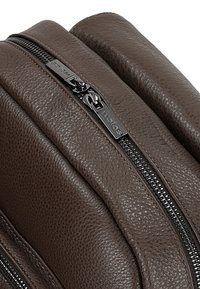 Braune Lederhandtasche mit strukturierter Oberfläche, ausgestattet mit zwei schwarzen Reißverschlüssen und glatten Kanten. Kompaktes und rechteckiges Design.