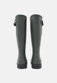 Botas verdes de borracha até ao joelho com uma textura suave, forma curva e um detalhe de correia de lado para ajuste. Branding discreto na sola.