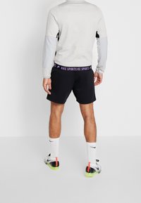 Haut de sport gris à manches longues avec des accents noirs, associé à un short noir avec une taille ornée d'un logo Nike violet et des chaussures vives avec des accents néon.