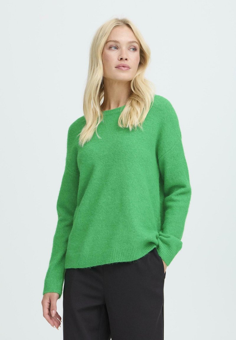 Groene gebreide trui met een ronde hals, lange mouwen en een ontspannen fit. Zachte textuur met ribgebreide zoom en manchetten. Gecombineerd met zwarte broek.