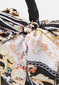Sac en tissu à motifs noir et blanc avec un détail en nœud, comportant des accents dorés et des designs complexes en orange et teal. Texture lisse.