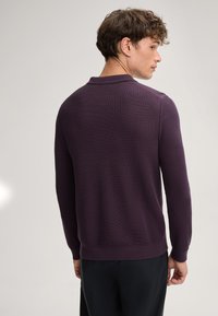Langer violetfarbener Polo-Pullover mit strukturiertem Stoff, gerippten Bündchen und Saum, mit einem klassischen Kragendesign. Sicht von hinten.