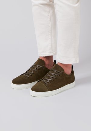Zapatillas de ante verde oliva con puntera redondeada, cordones grises y una suela de goma blanca. El diseño presenta acentos minimalistas y una textura suave.