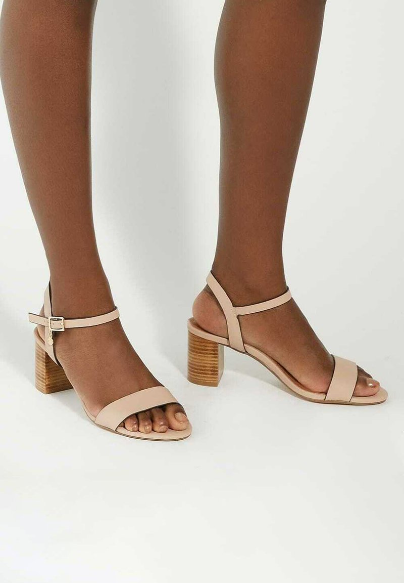 Beige, heeled sandals made of smooth leather featuring two straps across the foot and an adjustable ankle strap on a textured block heel.