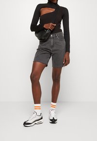 Černé tričko s dlouhými rukávy a výřezem, šedé džíny šortky, bílé tenisky s černými akcenty a bílé ponožky s oranžovými pruhy.