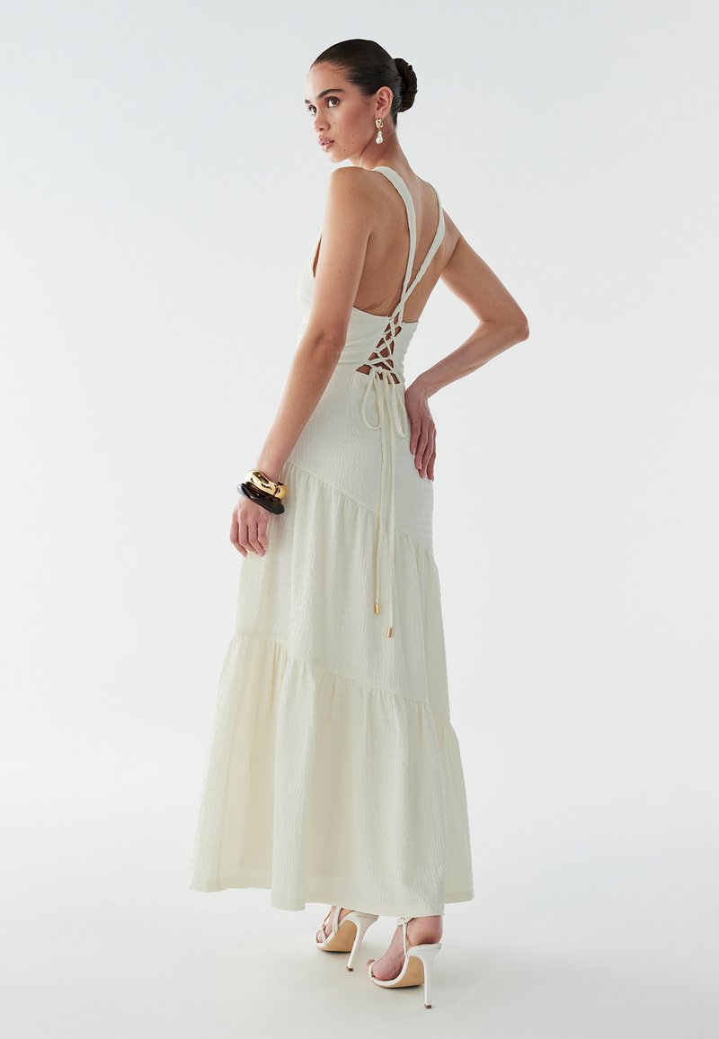 Maxi-jurk van licht crèmekleurige stof met getextureerde lagen, dunne bandjes, open rug met vetersluiting, gecombineerd met sandalen met hak.