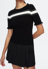 Camiseta de punto negra con Rayas blancas, con mangas cortas acampanadas y cuello redondo, combinada con una falda negra con pliegues.