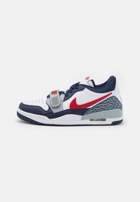 Nike sportcipők, fehér bőrből készült felső résszel, tengerészkék kiegészítőkkel, piros Swoosh logóval, szürke pánttal és szürke mintás sarokkal. Fehér középtalppal, látható légpárnával.
