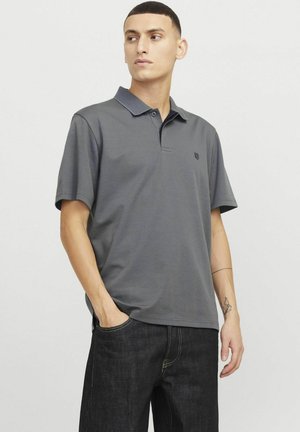 Polo shirt gris pour homme avec des manches courtes, un col et un petit emblème sur la poitrine. Le matériau semble lisse avec une texture subtile.