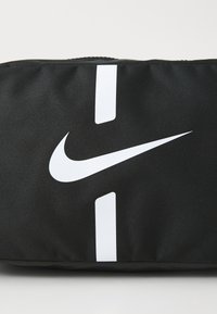 Schwarze Nike-Tasche mit einem weißen Swoosh-Logo und zwei vertikalen weißen Streifen, aus strapazierfähigem Stoff mit einer strukturierten Oberfläche.