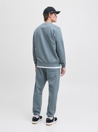 Pelēks sporta krekls un atbilstošas bikses, kas izgatavotas no mīksta materiāla. Iespējas ietver ribotu aproču, apaļu kakla izgriezumu un aizmugurējo kabatu. Melni sporta apavi ar baltām akcents.