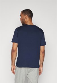 Camiseta azul marino de algodón con diseño de cuello redondo, manga corta y espalda lisa. Combinada con pantalones de chándal gris claro.
