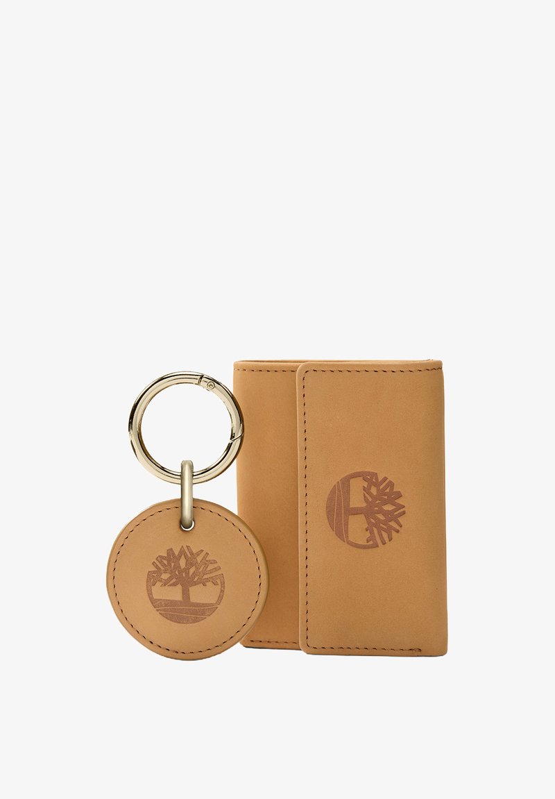 Conjunto de billetera y llavero de cuero marrón con un logotipo de árbol en relieve. La billetera tiene un diseño elegante; el llavero incluye un disco redondo y un anillo de metal.