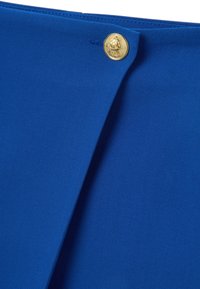 Tessuto blu royal con una superficie liscia, caratterizzato da un bottone dorato con un emblema. Il tessuto è confezionato con una piega ordinata.