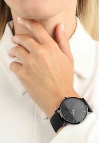 Schwarze analoge Armbanduhr mit rundem Ziffernblatt, minimalistischer Gestaltung und schwarzem Silikonarmband. Verfügt über silberne Stundenmarker und eine einfache Krone.