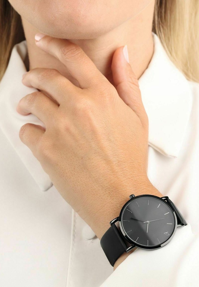 Schwarze analoge Armbanduhr mit rundem Ziffernblatt, minimalistischer Gestaltung und schwarzem Silikonarmband. Verfügt über silberne Stundenmarker und eine einfache Krone.