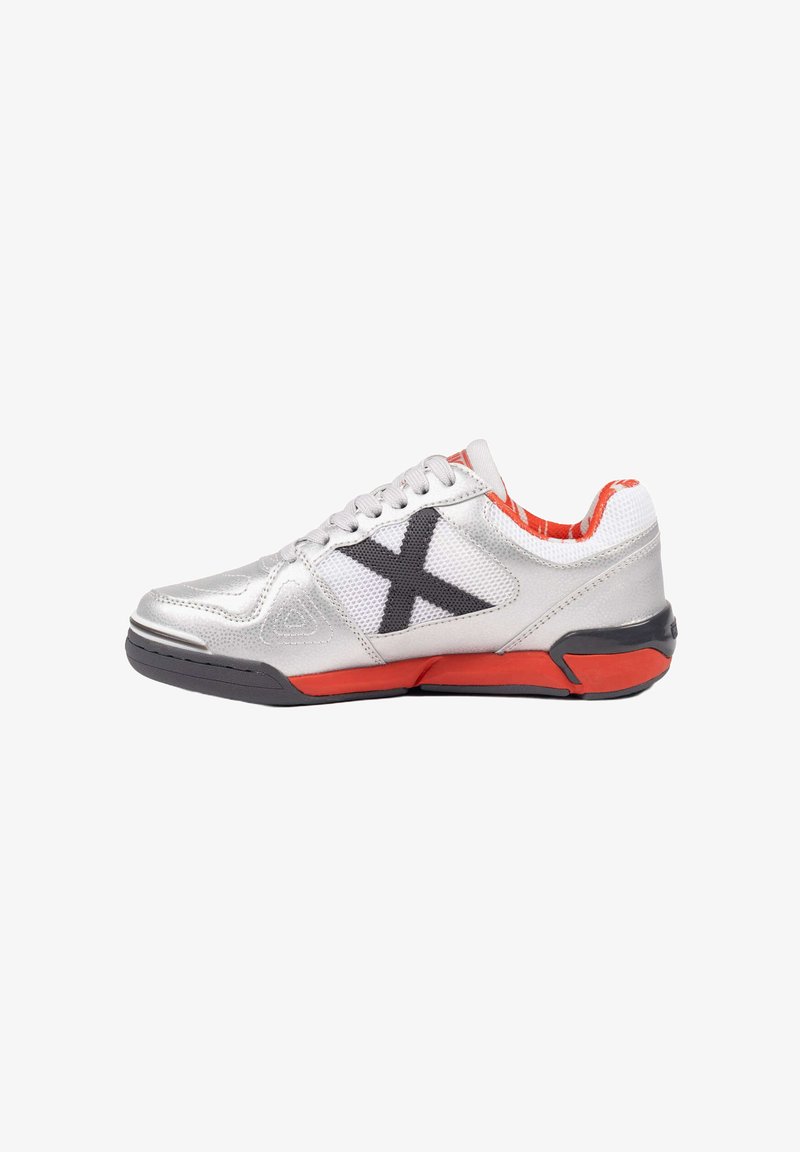 Zapatilla deportiva plateada con una "X" negra en el costado, detalles rojos en la suela y el forro interior, y cordones blancos.