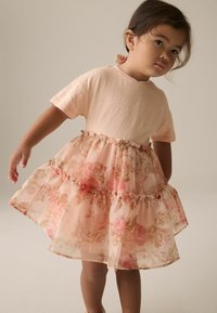 Blumenkleid mit einem leicht rosa Baumwolloberteil, sheer geschichtetem Rock mit Rosenmustern und einer rüschierten Taillenapplikation.