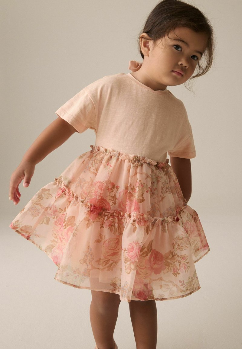 Blumenkleid mit einem leicht rosa Baumwolloberteil, sheer geschichtetem Rock mit Rosenmustern und einer rüschierten Taillenapplikation.