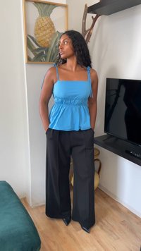 Helles blaues, dehnbares Top mit quadratischer Ausschnitt und verstellbaren Trägern; kombiniert mit hochgeschnittenen, schwarzen Weitbein-Hosen und spitzen schwarzen Schuhen.