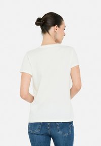 Camiseta blanca de manga corta con cuello redondo, hecha de algodón, con un corte holgado y textura suave, combinada con jeans de mezclilla azul.