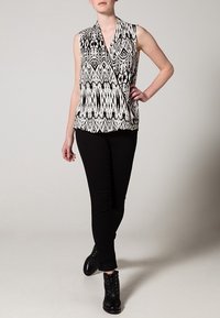 Czarny i biały bezrękawnik o kroju kopertowym, z wygrawerowanymi wzorami geometrycznymi; zestawiony z czarnymi spodniami i botkami za kostkę.
