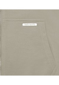 Light olive green zip-up hoodie featuring a soft texture, side pocket, and silver "bazirx republiq" logo tag on the front.