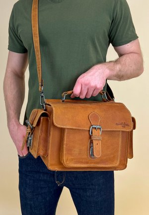 Leather messenger bag in tan, featuring a flap closure, front pocket, and metal hardware. The design includes contrast stitching and a shoulder strap.